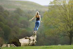 A woman balances on her tip-toes, leaning off the edge of a large log